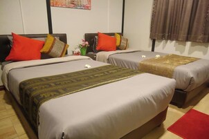 Habitación de hotel con dos camas, cada una con una colcha estampada y varias almohadas. Hay una mesita con un jarrón de flores y una alfombra roja en el suelo.