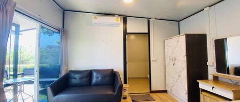 A modern room with a black leather sofa, a bed, a wooden desk, and a large mirror.