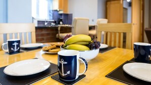 Una mesa de comedor con platos, un cuenco de fruta y tazas de café.
