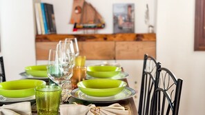 A dining table with green plates and clear glasses, a wooden cabinet in the background, and a black chair.