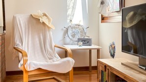 Une pièce chaleureuse avec une chaise en bois recouverte d’une couverture blanche, une petite table ornée d’un objet décoratif et un téléviseur posé sur un meuble en bois.
