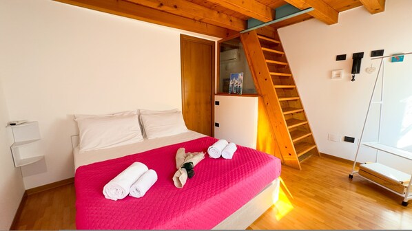 A bedroom with a bed, a wooden ladder, a white wall, and a window.
