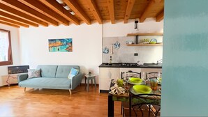 Un salon avec un canapé, une table à manger dressée pour deux personnes et un coin cuisine équipé d’une cuisinière et d’étagères.