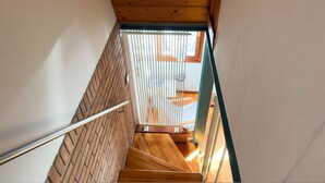 Un escalier en bois avec une rampe métallique, menant à une pièce dotée d’une fenêtre et d’un lit.