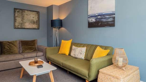 A modern living room with a sofa, a coffee table, a lamp, and artwork on the walls. - Stylish 3 bedroom house with parking and private garden. Ideal for families, groups or work stays. (Cheltenham)