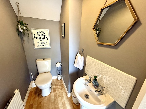 A bathroom with a toilet, sink, and mirror. There is a sign on the wall that reads "Wash your hands, you filthy animal."