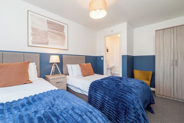 A hotel room with two beds, a nightstand, a lamp, a painting, and a wardrobe.
