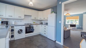 A modern kitchen with white cabinets, a washing machine, an oven, and a refrigerator. - Stylish 3 bedroom house with parking and private garden. Ideal for families, groups or work stays. (Cheltenham)