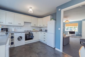 Een moderne keuken met witte kasten, een wasmachine, oven en koelkast.