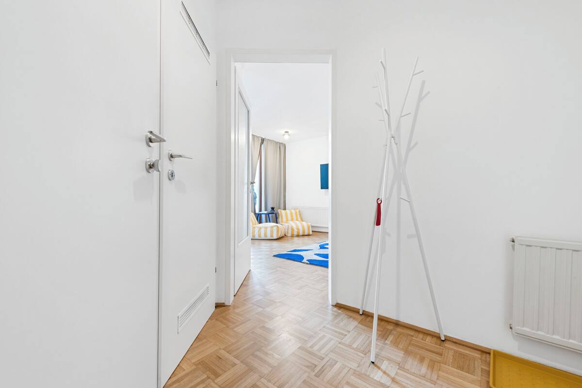 Un pasillo con piso de madera, paredes blancas y una puerta con picaporte moderno.