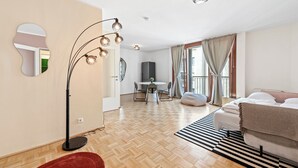 A modern hotel room with a wooden parquet floor, a bed with a striped rug, a dining area with a table and chairs, a kitchen area, and a large mirror on the wall. - 4ty3-Apartments Naschmarkt City Apt (Vienna)