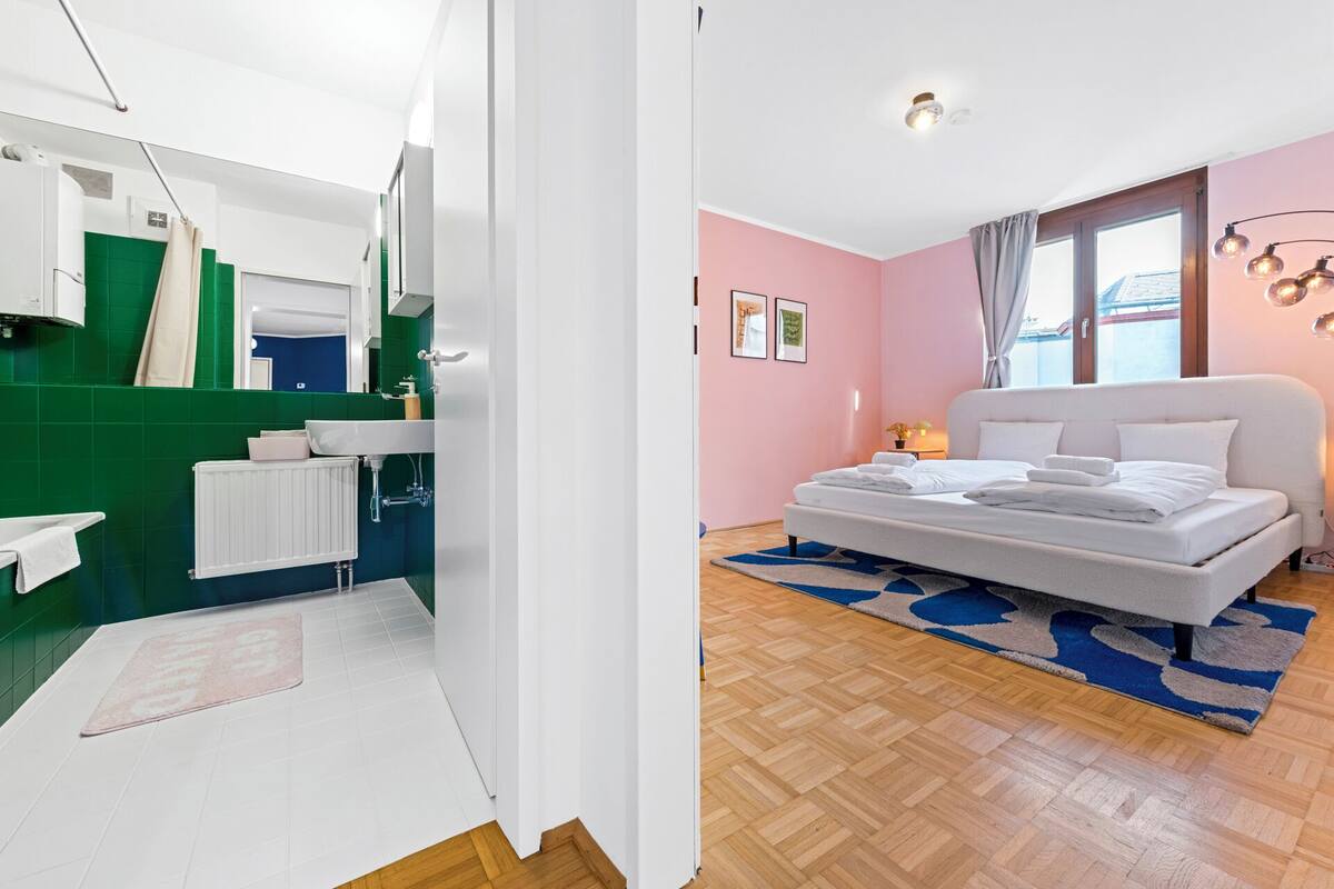 Habitación de hotel moderna con una cama grande, baño con azulejos verdes y vistas a la ciudad.
