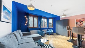 A modern living room with a blue accent wall, a grey sofa, a coffee table, and a dining area with a high chair and a table. - 4ty3-Apartments Naschmarkt City Apt (Vienna)