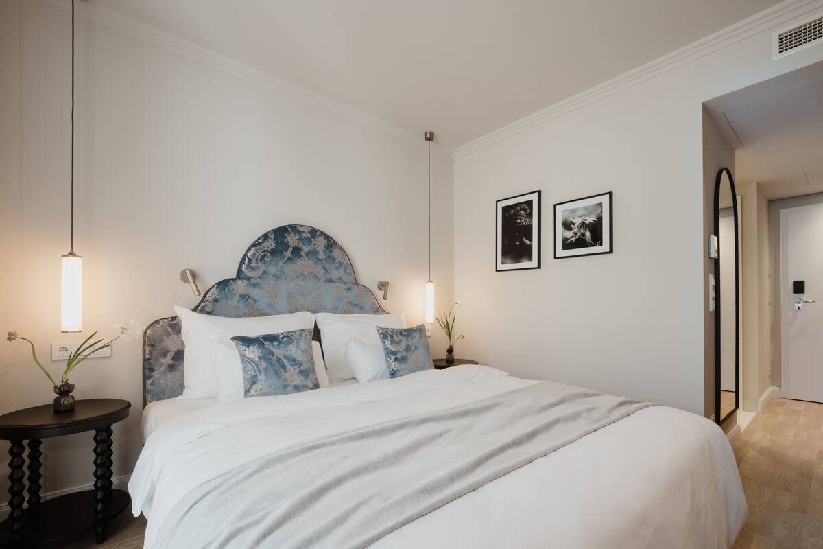 A neatly arranged bedroom with a large bed, bedside tables, and wall-mounted artwork.