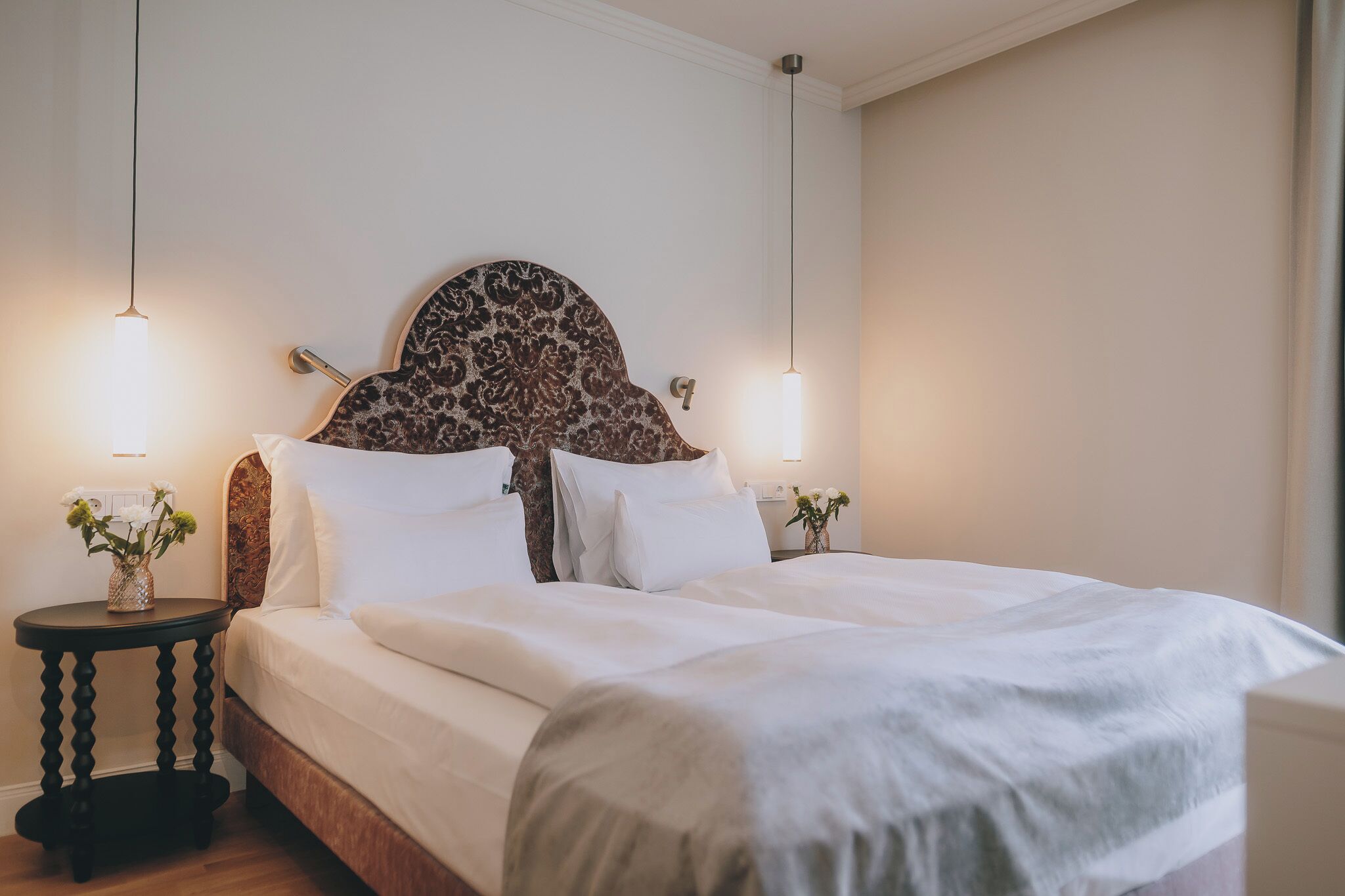 A neatly made bed with a patterned headboard, two bedside tables with lamps, and a vase with flowers on one table.