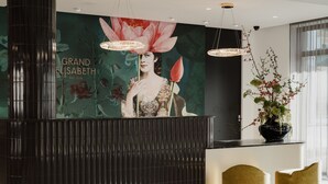 A reception area with a dark reception desk, a large floral mural, and two gold chairs. - Grand Elisabeth (Bad Ischl)