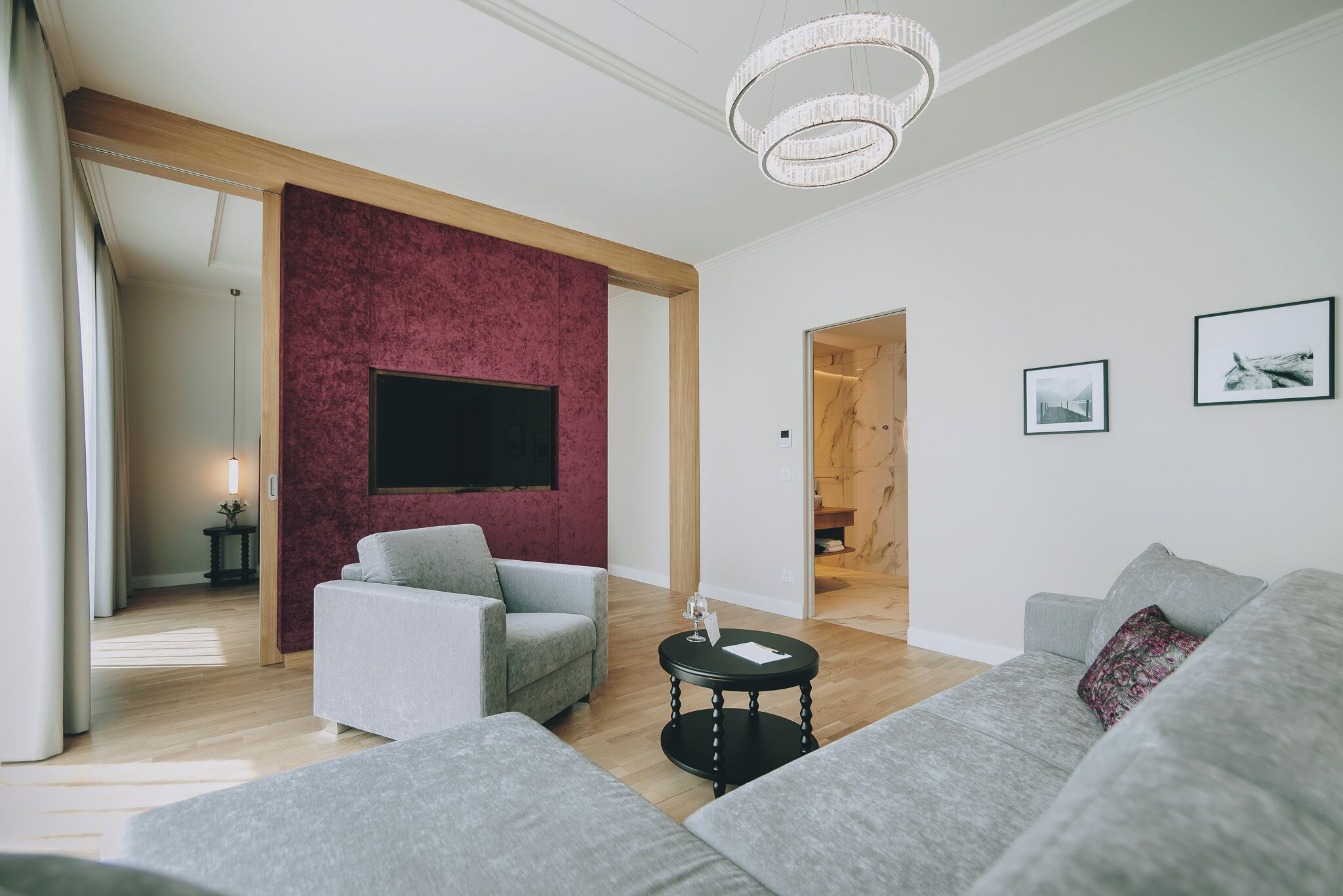 Un salon moderne avec des canapés gris, un téléviseur à écran plat, un lustre et des tableaux encadrés accrochés au mur.