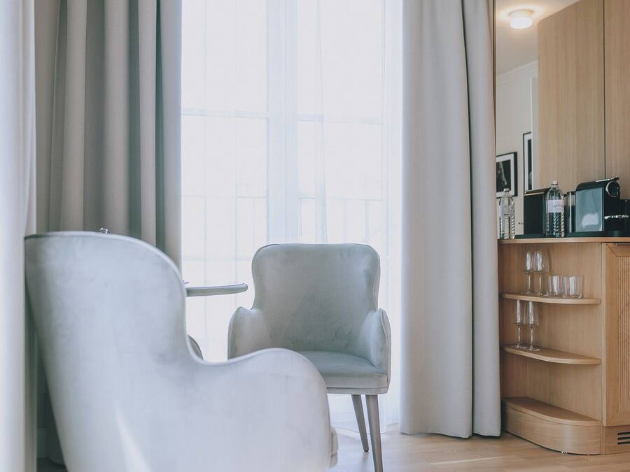 Un saló modern amb un relaxant gris clar, un armari de fusta amb electrodomèstics de cuina i una finestra gran amb cortines translúcides.