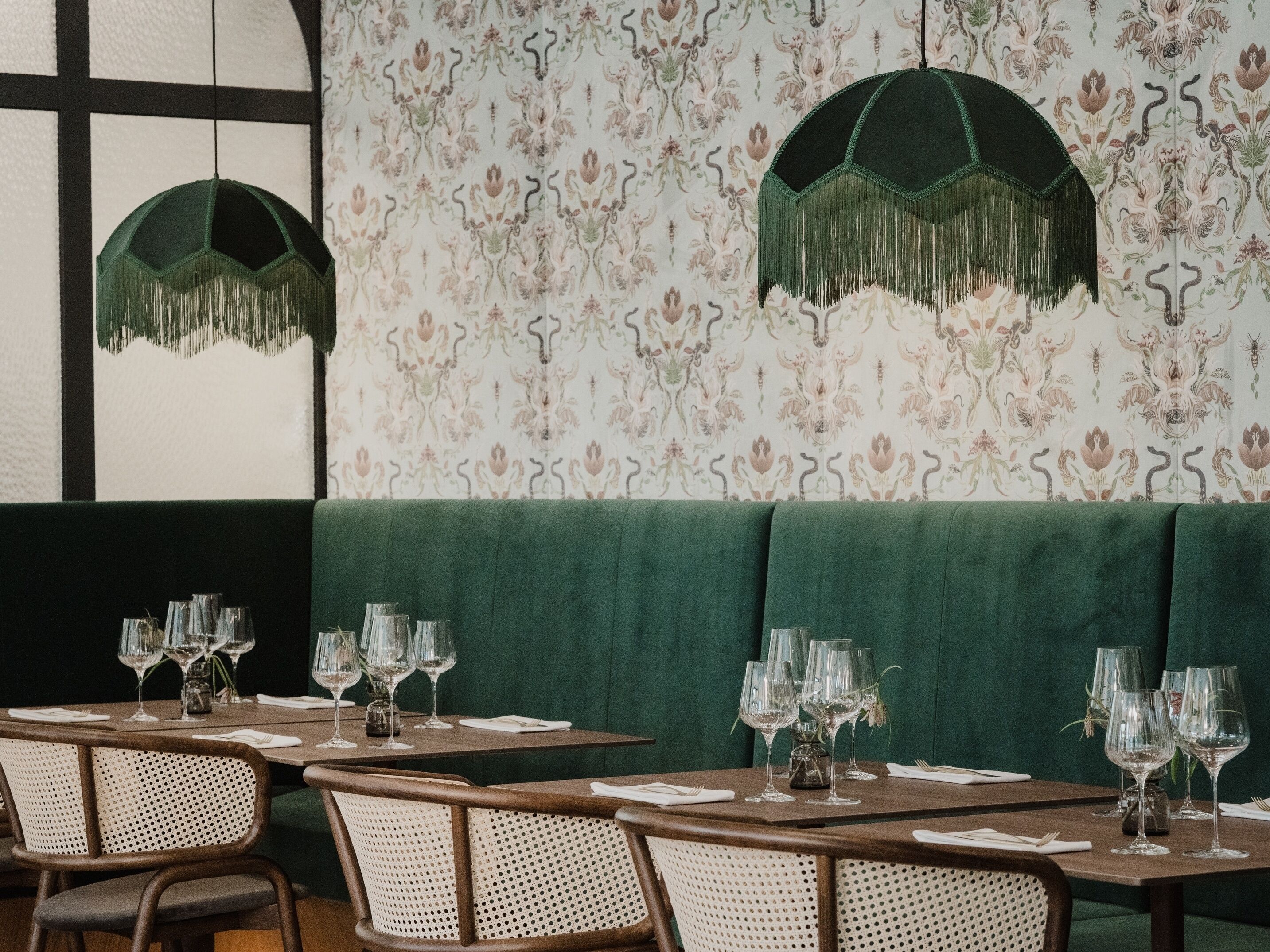 Ein Restaurantinneres mit grün gepolsterten Sitzmöglichkeiten, Holztischen und floralem Wandpapier.