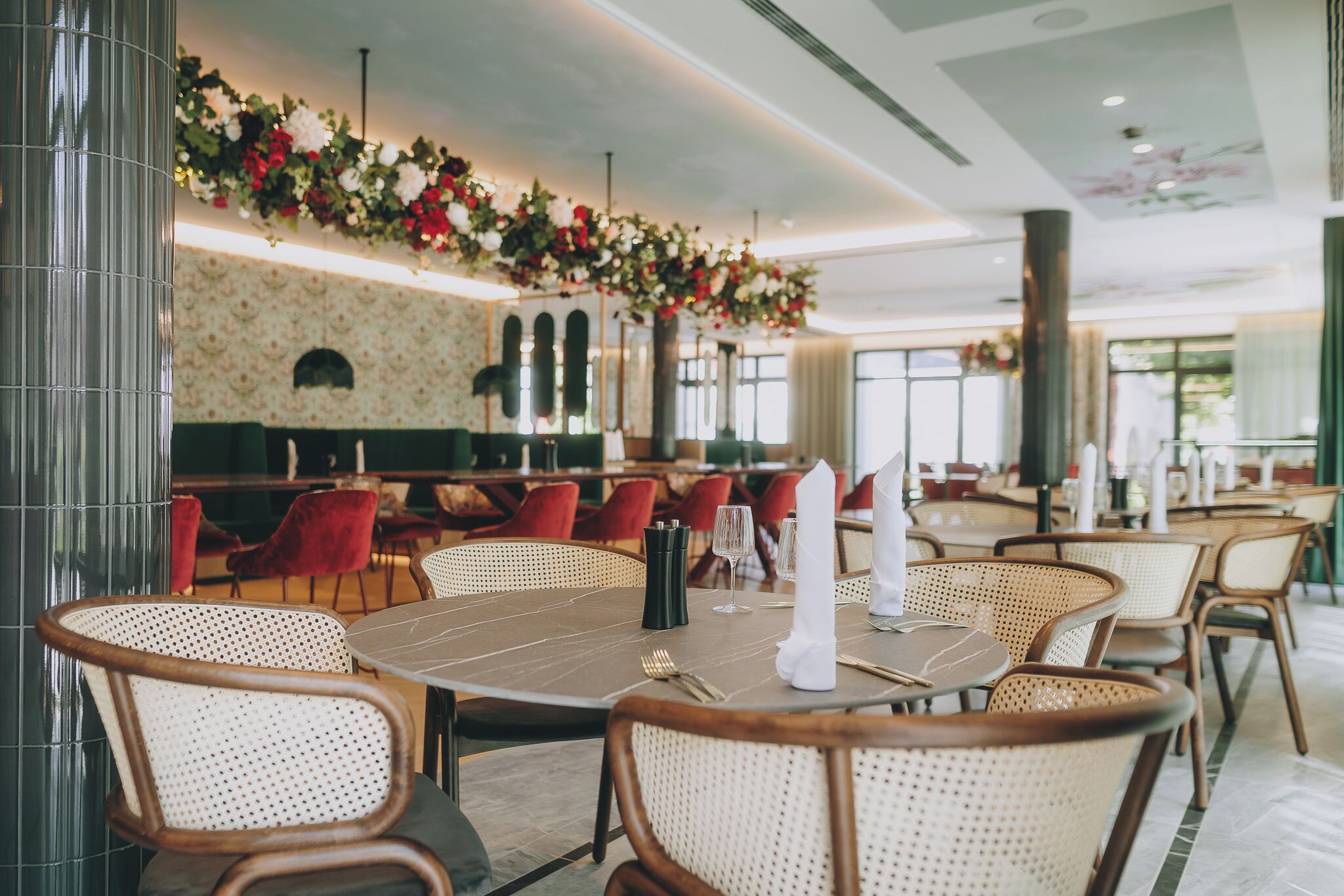 A restaurant with round tables, wicker chairs, and red upholstered chairs.