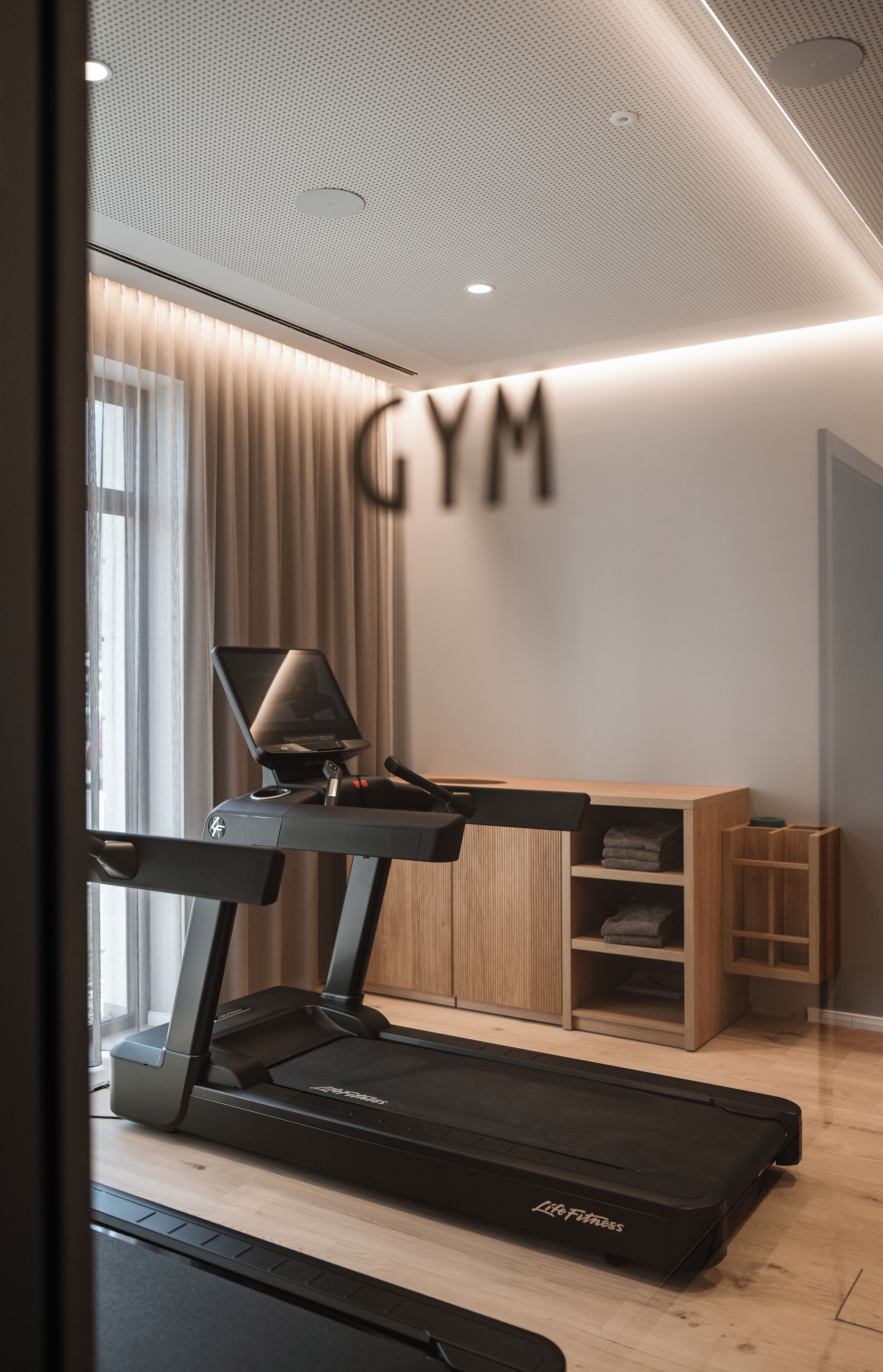 Un gimnasio moderno con cinta de correr, bicicleta estática de pared y un mueble de madera.