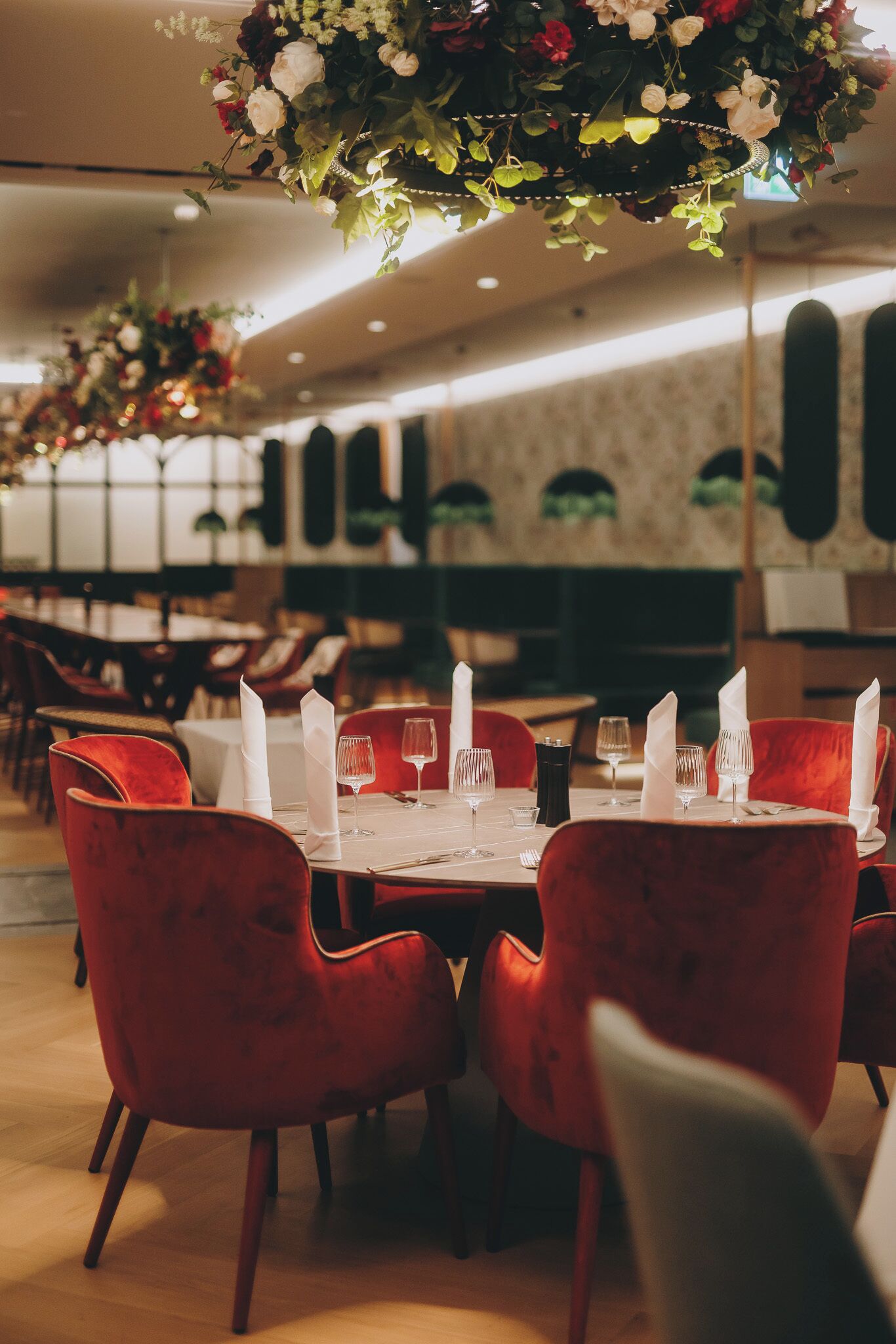 A restaurant with red velvet chairs, white napkins, and a floral centerpiece on the tables.