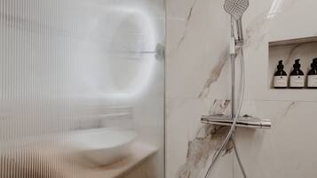 A modern bathroom with a shower, a glass door, and a marble wall. There are three bottles of toiletries on the wall.