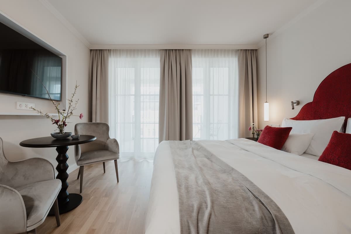 A hotel room with a bed, a desk, a chair, a TV, and a window with curtains.