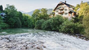 A riverside hotel with a view of a flowing river, surrounded by lush greenery and mountains in the background.