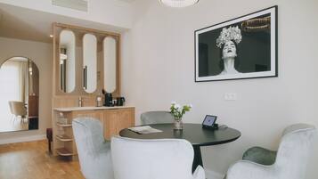 A modern dining area with a round table, white chairs, and a vase with flowers. There is a framed artwork on the wall and a wooden cabinet with mirrors.