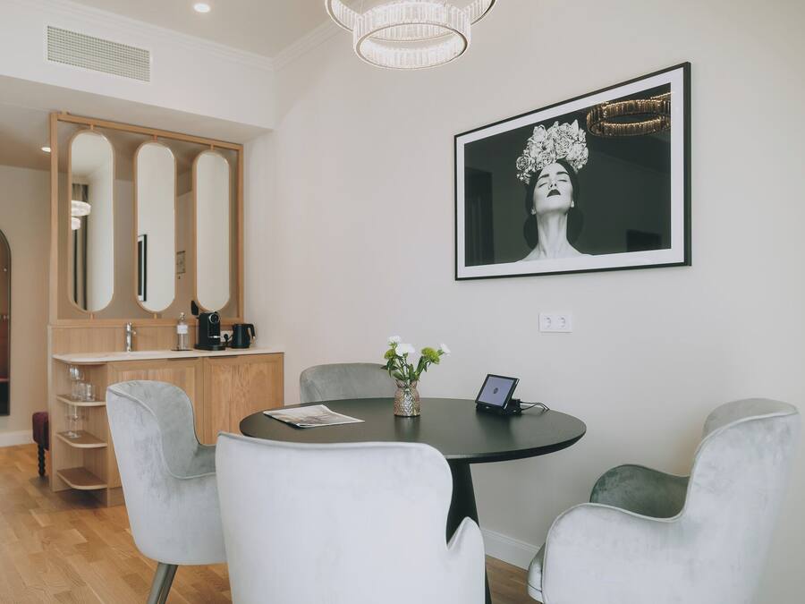 A modern dining area with a round table, white chairs, and a vase with flowers. There is a framed artwork on the wall and a wooden cabinet with mirrors.