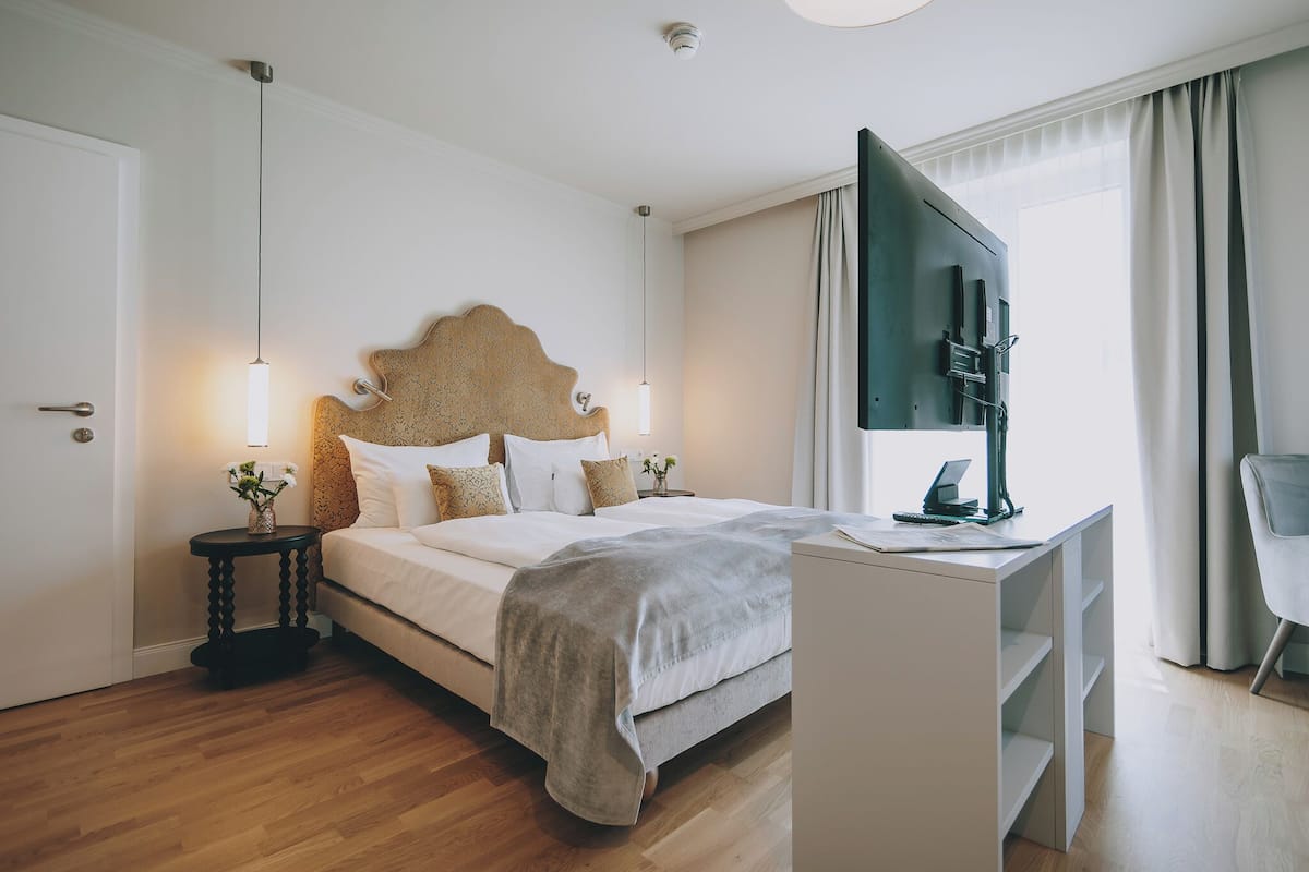 A modern hotel room with a large bed, a desk with a flat-screen TV, and a chair.
