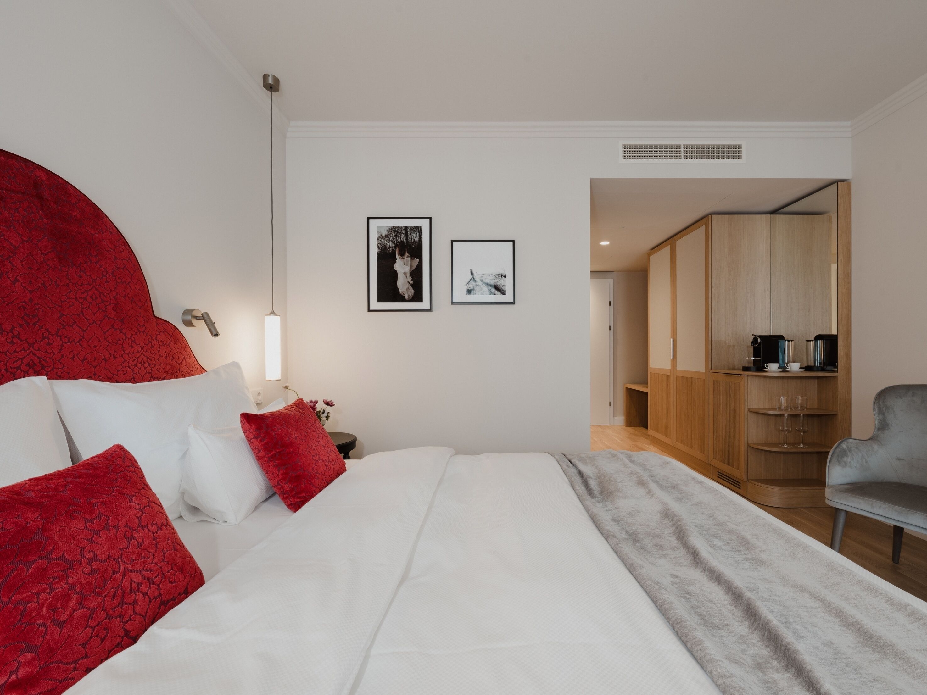 A modern hotel room with a large bed, a wardrobe, a seating area, and a kitchenette.