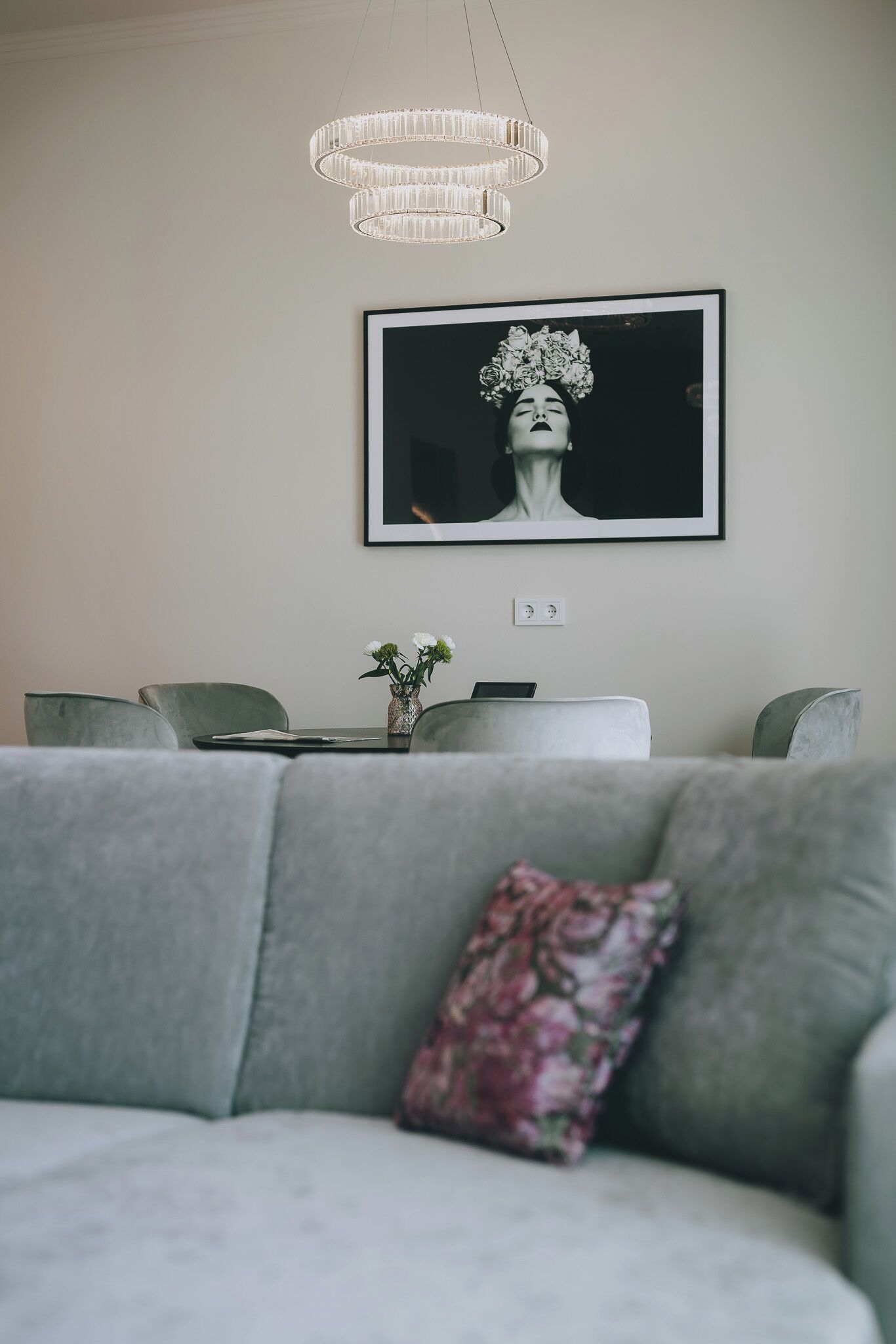 A modern living room with a grey sofa, a decorative pillow, a framed artwork on the wall, and a chandelier.
