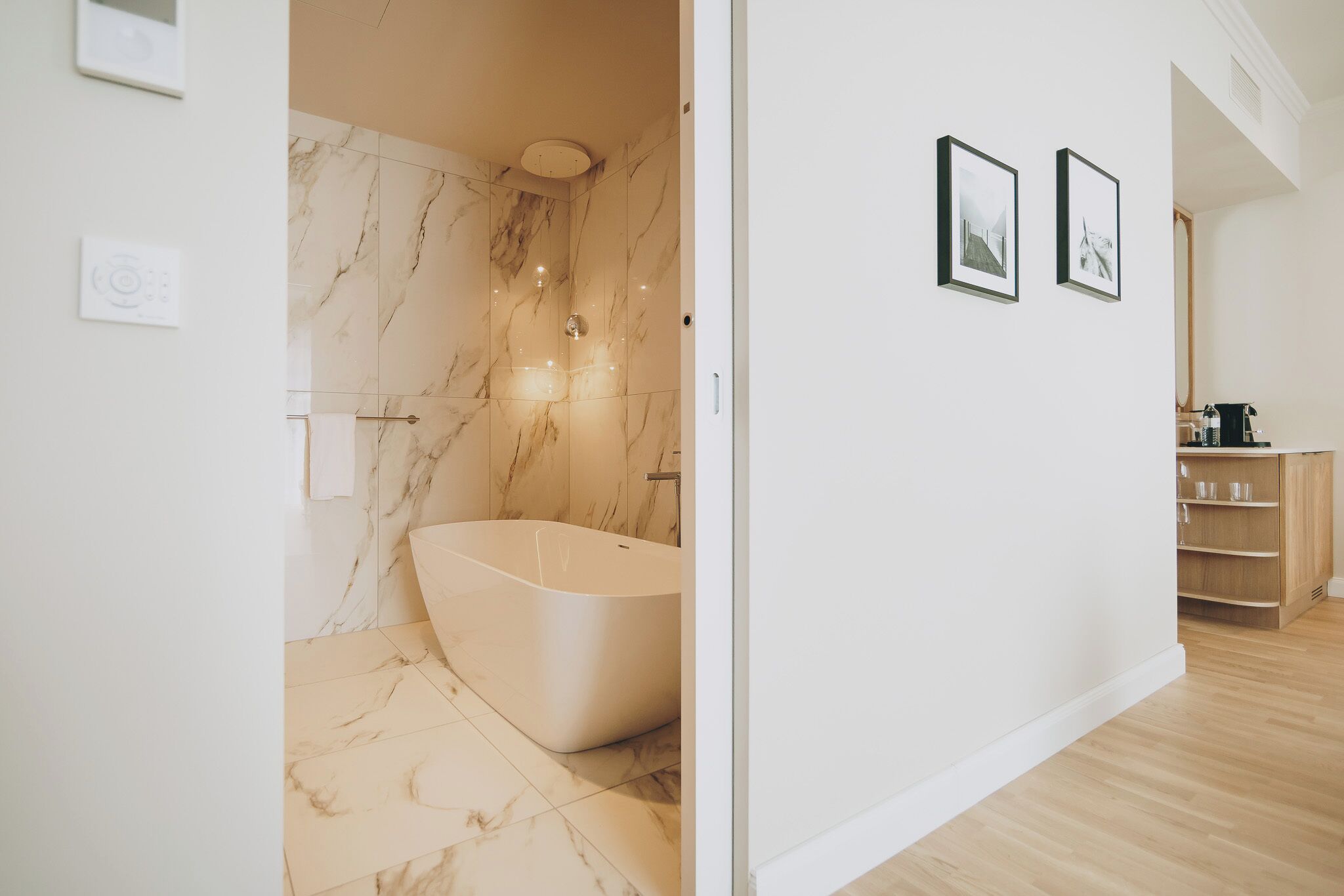 A modern bathroom with a freestanding bathtub, marble walls, and a wooden vanity.