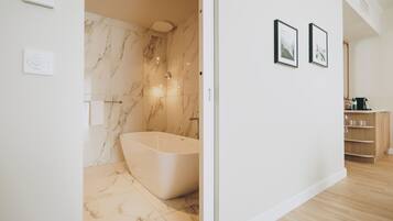 A modern bathroom with a freestanding bathtub, marble walls, and a wooden vanity.