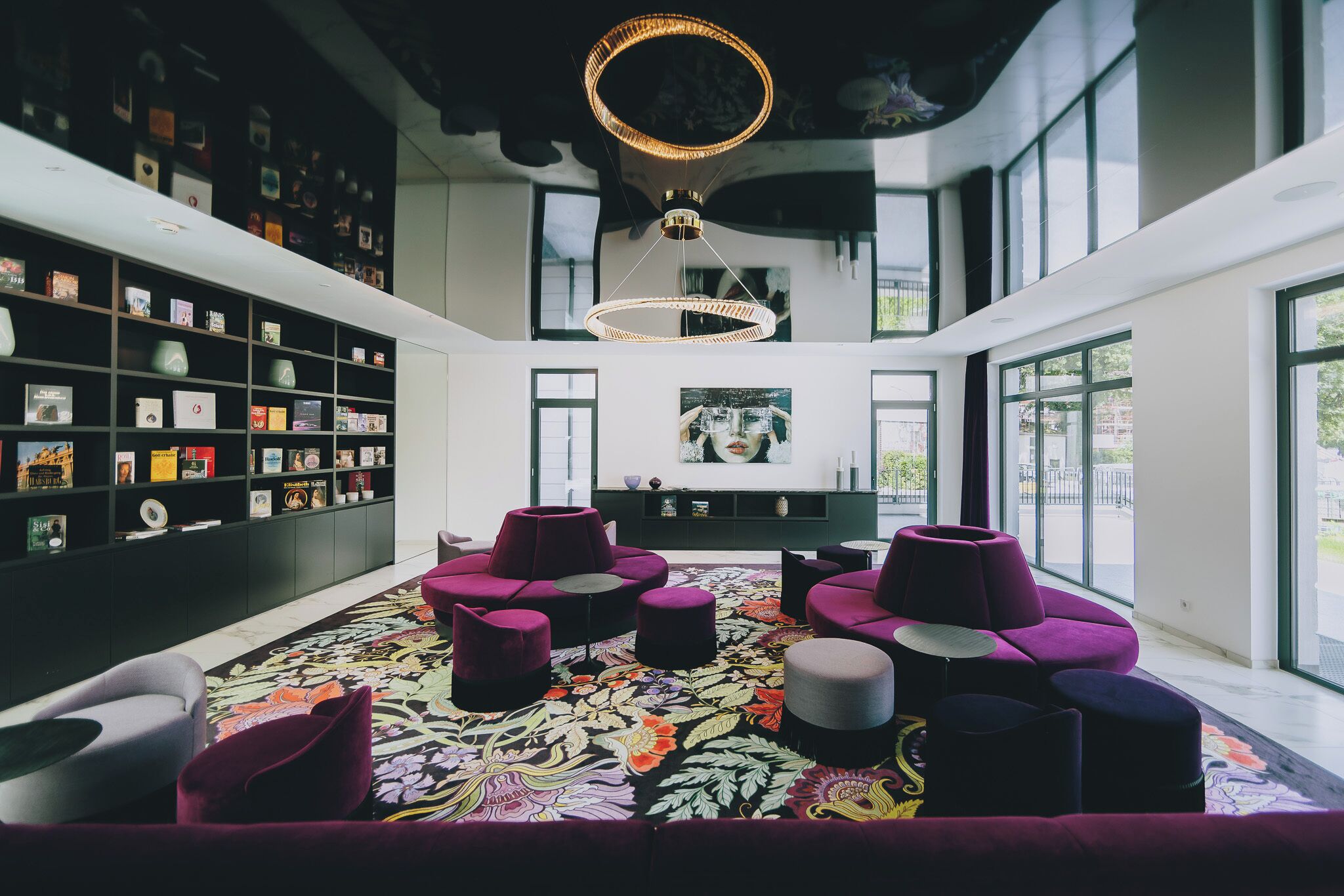 A modern reading room with a large bookshelf, comfortable seating, and large windows.