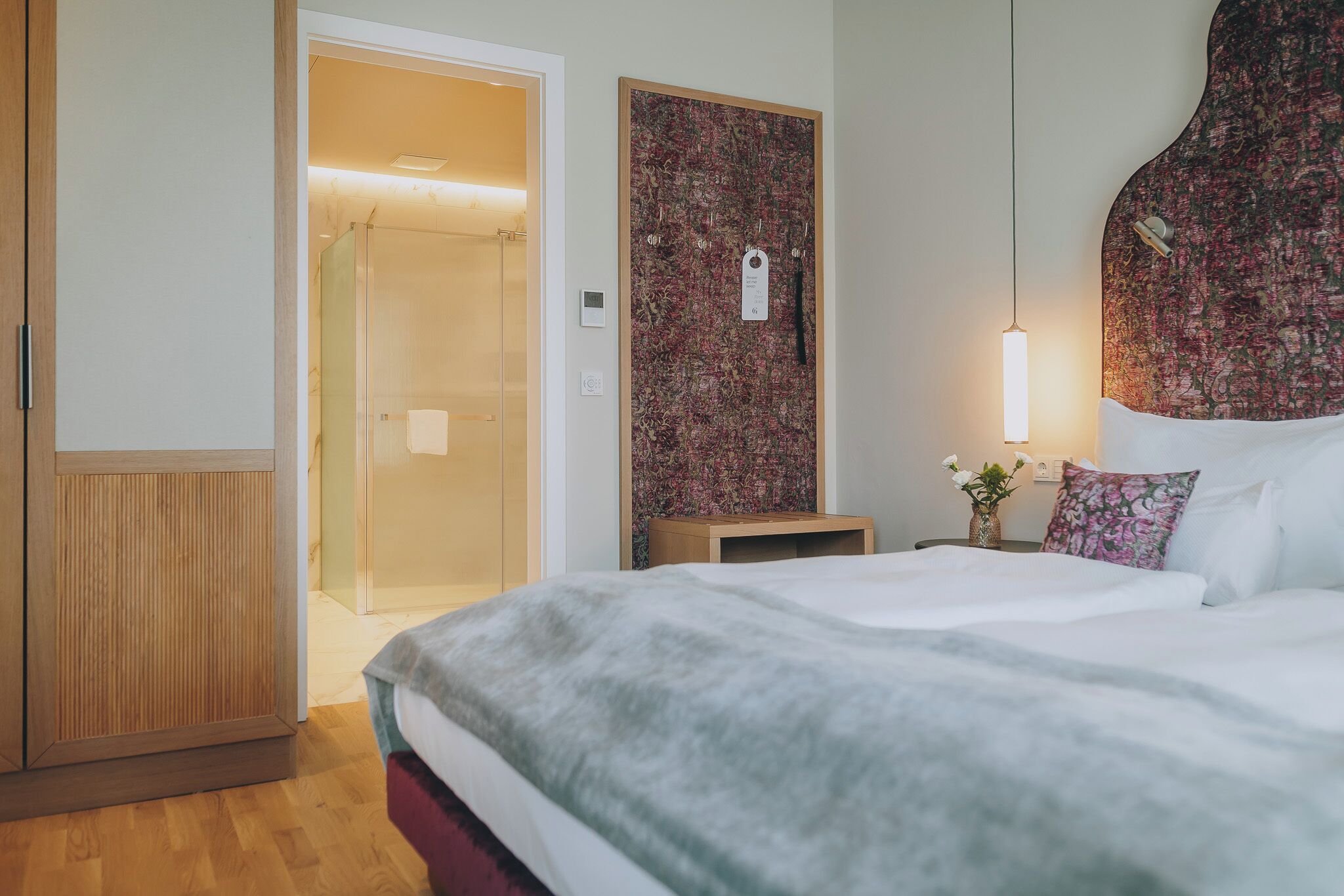 A hotel room with a bed, a wardrobe, a shower area, and a wall with a floral pattern.