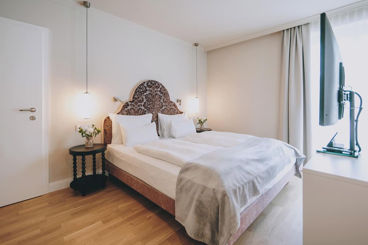 A neatly arranged bedroom with a large bed, two bedside tables, a wall-mounted TV, and a window with curtains.