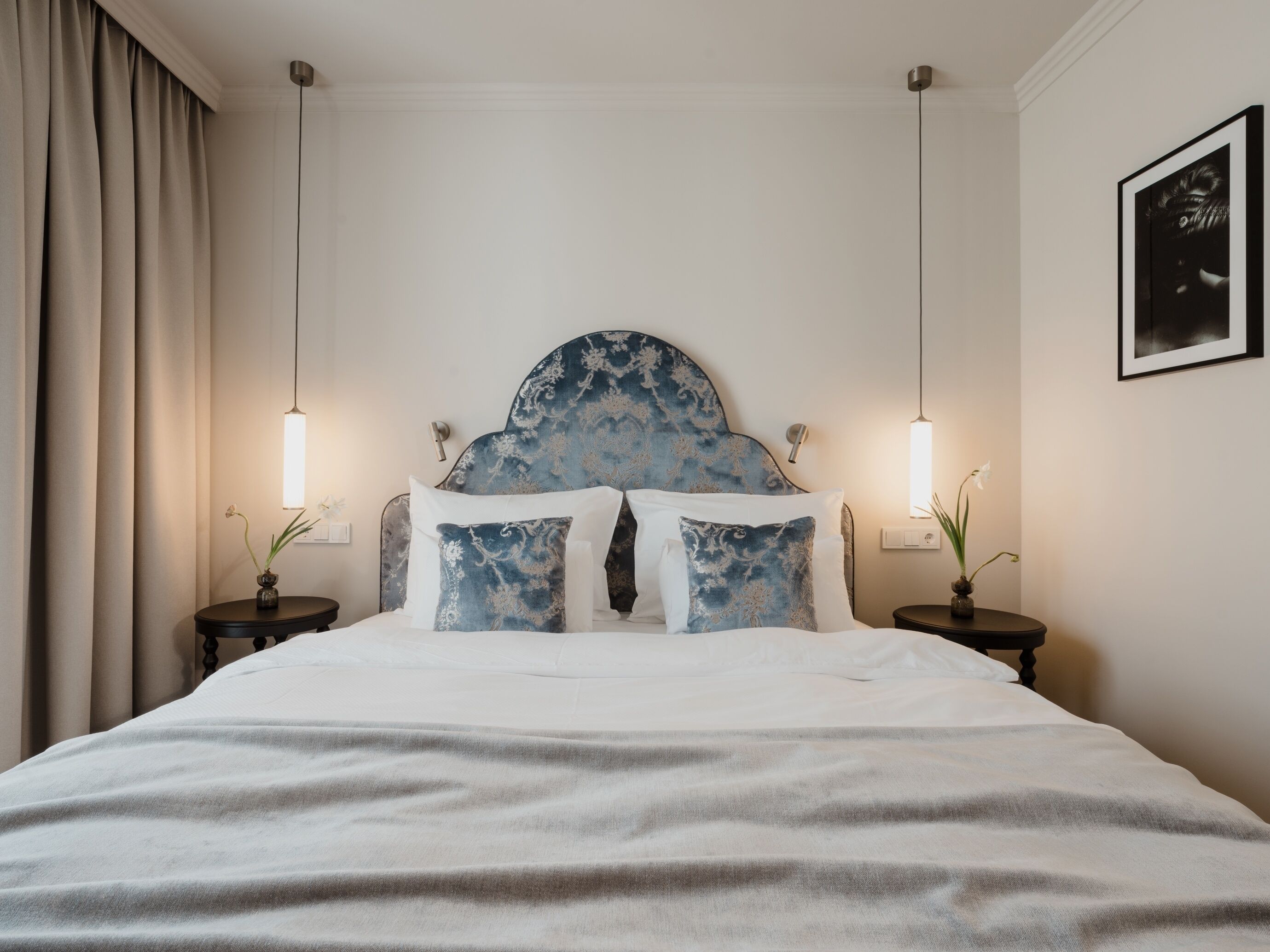 A neatly made bed with a blue headboard, two bedside tables with lamps, and a framed picture on the wall.