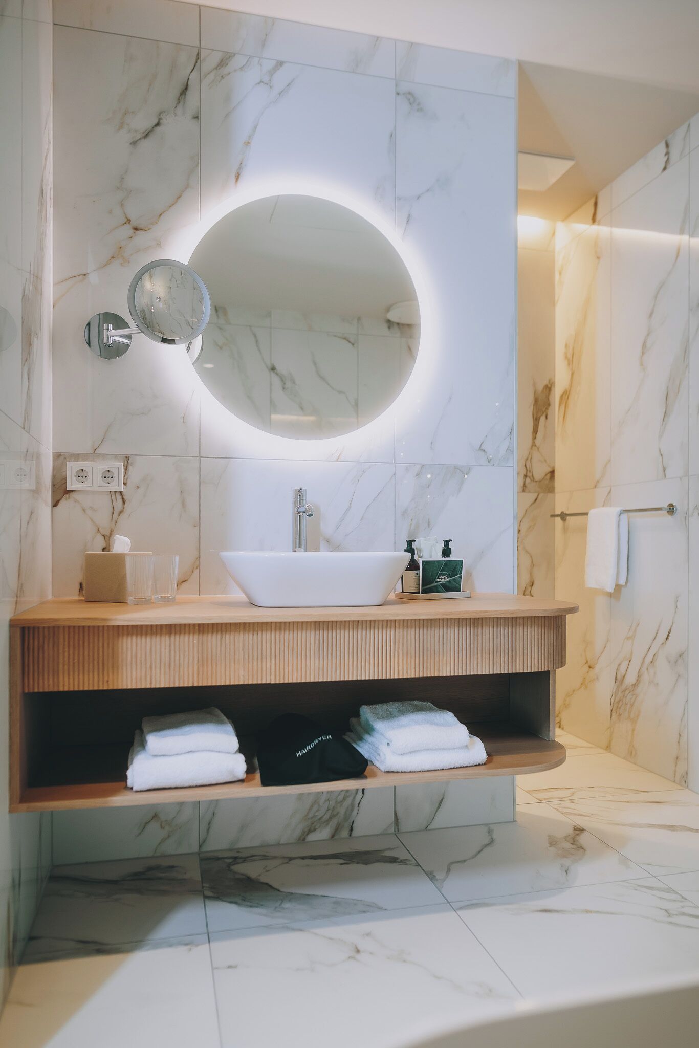 A modern bathroom with a marble vanity, a large mirror, and a towel rack.