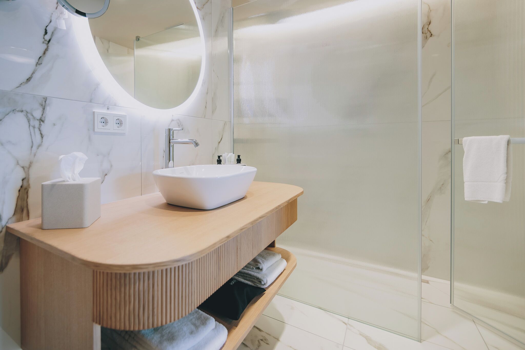 Une salle de bain moderne avec un meuble-lavabo en marbre, une cabine de douche en verre et un porte-serviettes.