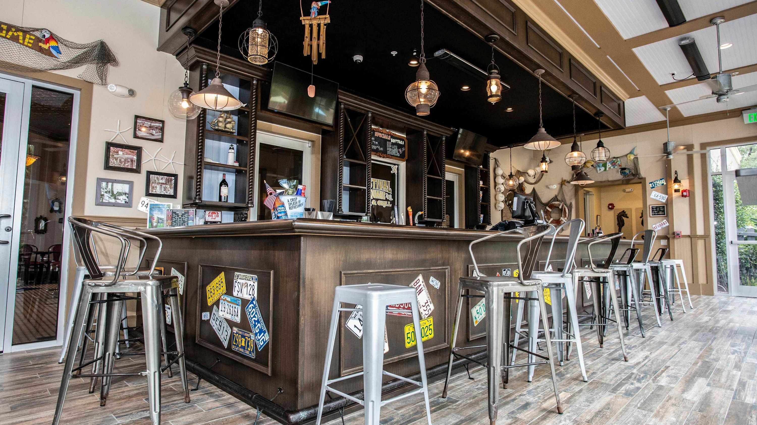 Un área de bar con mostrador de madera, taburetes de metal y lámparas colgantes.