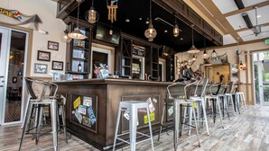 A bar area with a wooden counter, metal bar stools, and hanging pendant lights.