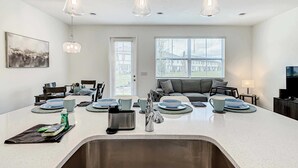 A modern kitchen with a central island, a dining area with chairs, a sofa, and a television.