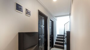 Um corredor com um refrigerador preto, uma porta com placa de identificação e uma escada que leva a um andar superior.