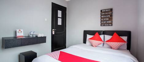A hotel room with a bed, a black door, a wall-mounted shelf with toiletries, and a sign listing man rules.