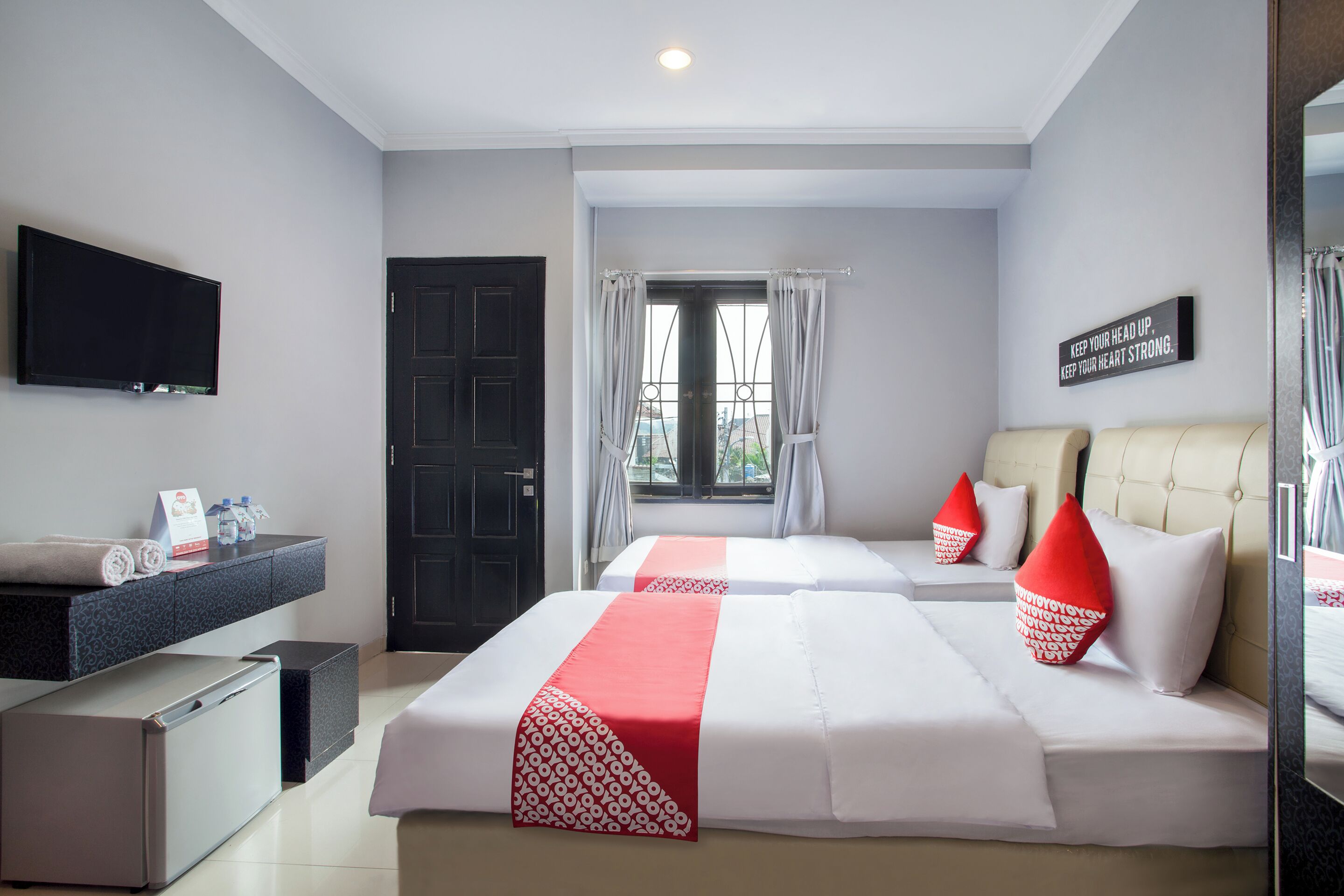 A hotel room with two beds, a TV, a minibar, and a window with curtains.