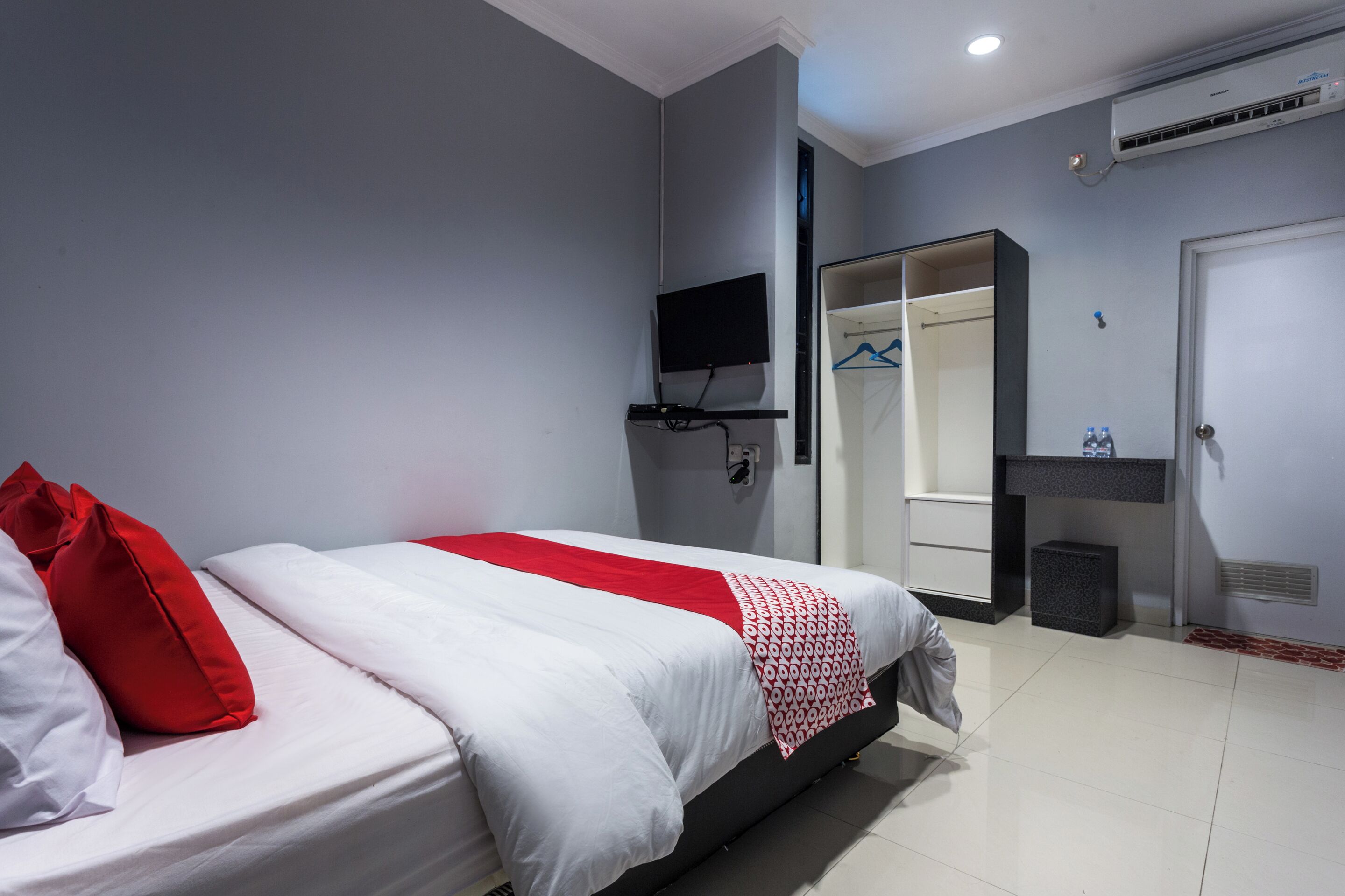 Een hotelkamer met een bed, een aan de muur bevestigde televisie, een kledingkast en een kleine prullenbak.