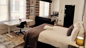 A modern bedroom with a large bed, a desk, and a TV.